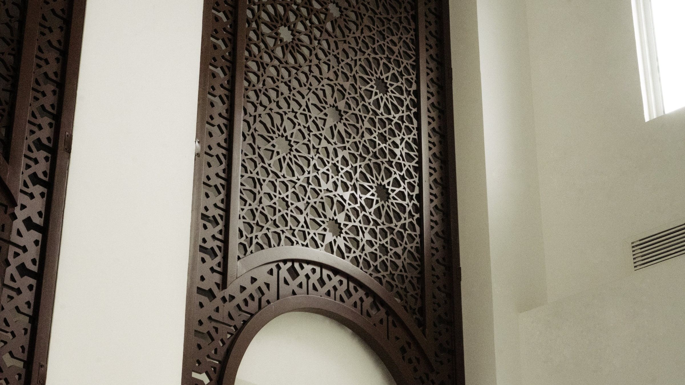 Dark timber lattice screen with a carved geometric star pattern above an arched opening inside Masjid Baru RPN Kg Rimba