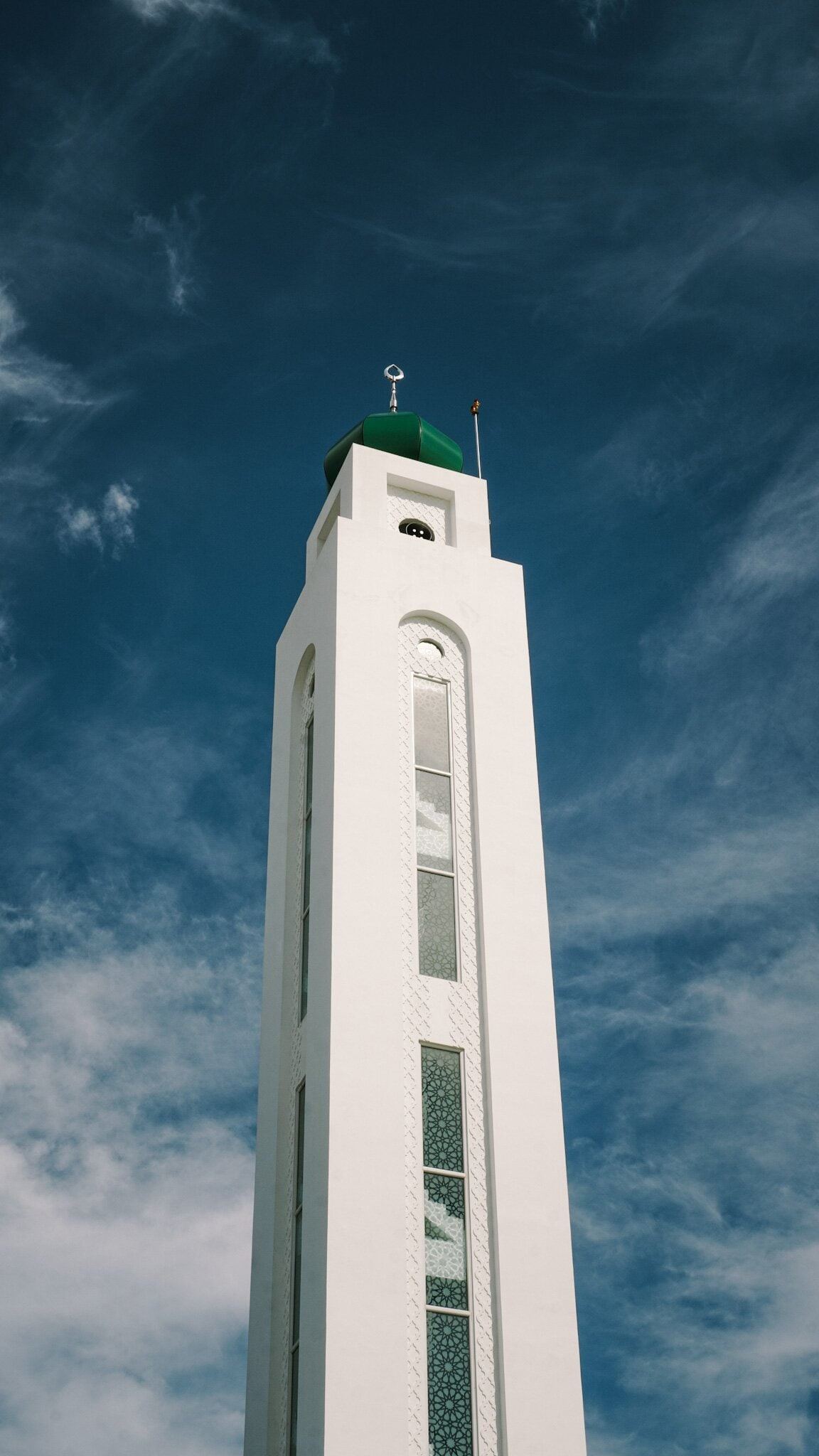 White minaret of Masjid Baru RPN Kg Rimba with a green dome, patterned glazing and a crescent finial against a blue sky