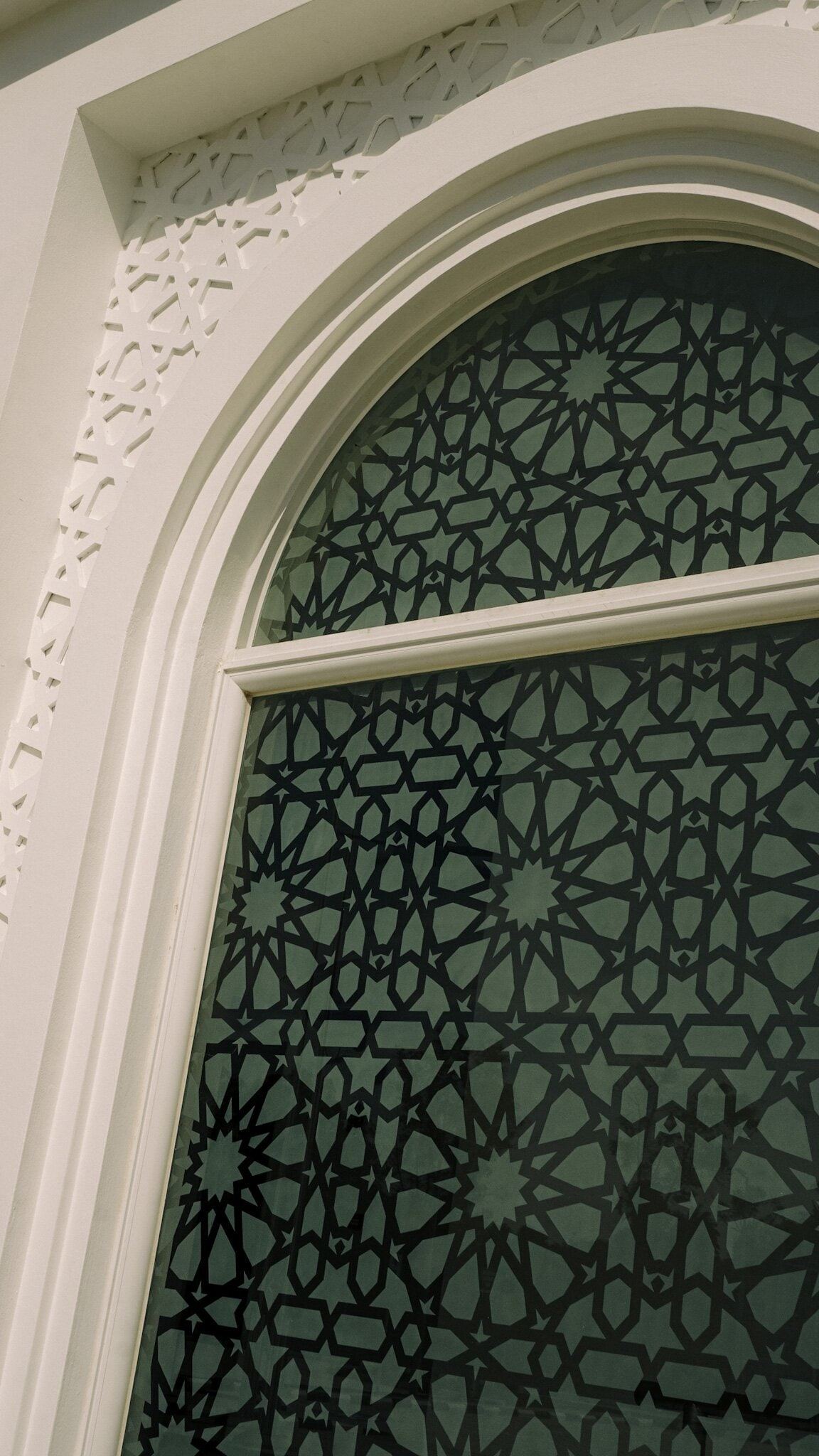 Arched window at Masjid Baru RPN Kg Rimba with geometric star-pattern glazing and a carved plaster border